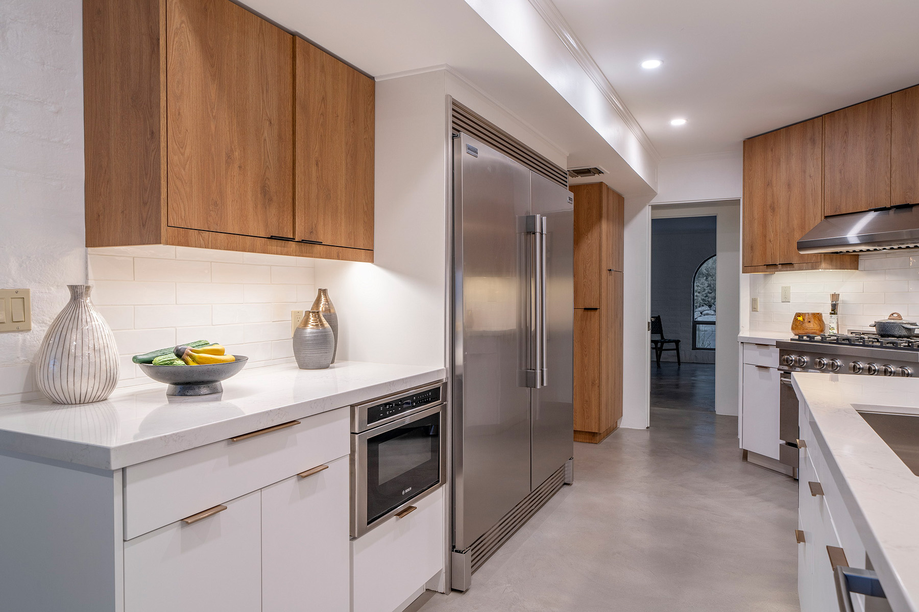 Bright kitchen showcasing custom wood and white cabinetry, quartz countertops, stainless steel refrigerator and range, subway tile backsplash, and clean modern finishes.