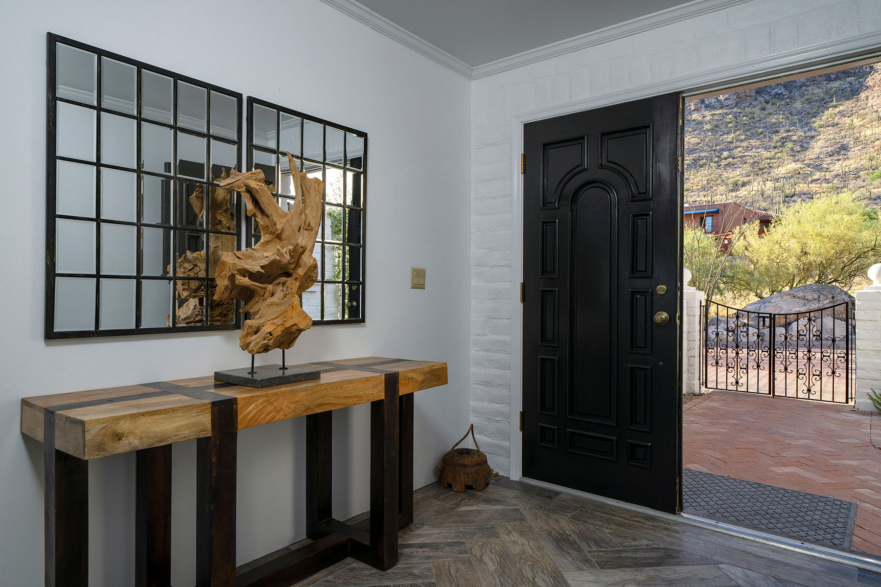 Entry foyer featuring a black arched front door, decorative mirrors, sculptural wood artwork, white-painted brick walls, and views into the landscaped courtyard.