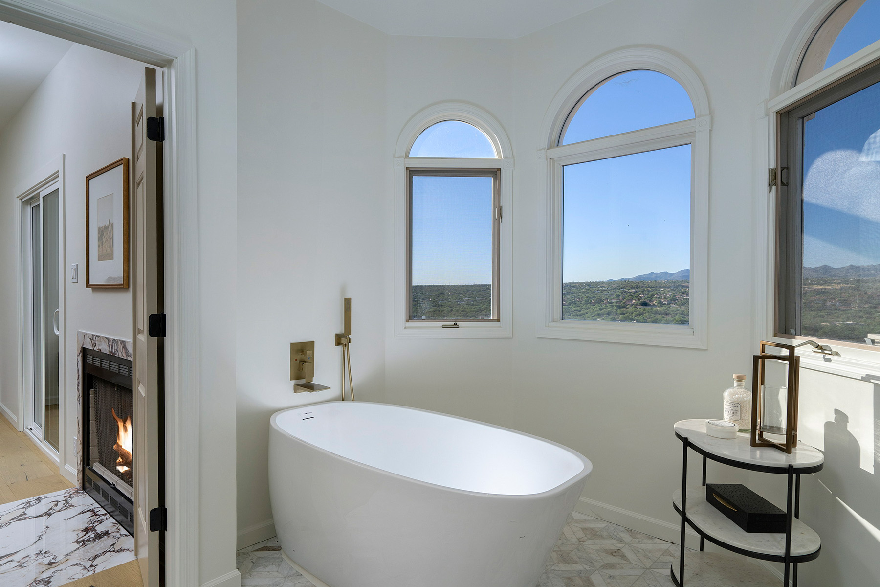 Thoughtfully renovated luxury bathroom featuring a freestanding soaking tub, arched windows, and panoramic mountain views in an Oro Valley home by Casa Garcia Morse