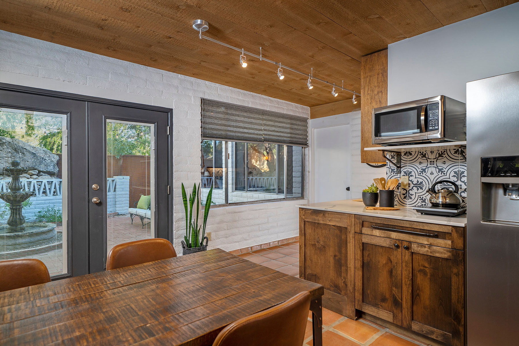 Cozy dining area featuring wood cabinetry, wood-plank ceiling, terracotta tile flooring, leather dining chairs, and views to the courtyard through large windows and glass doors.