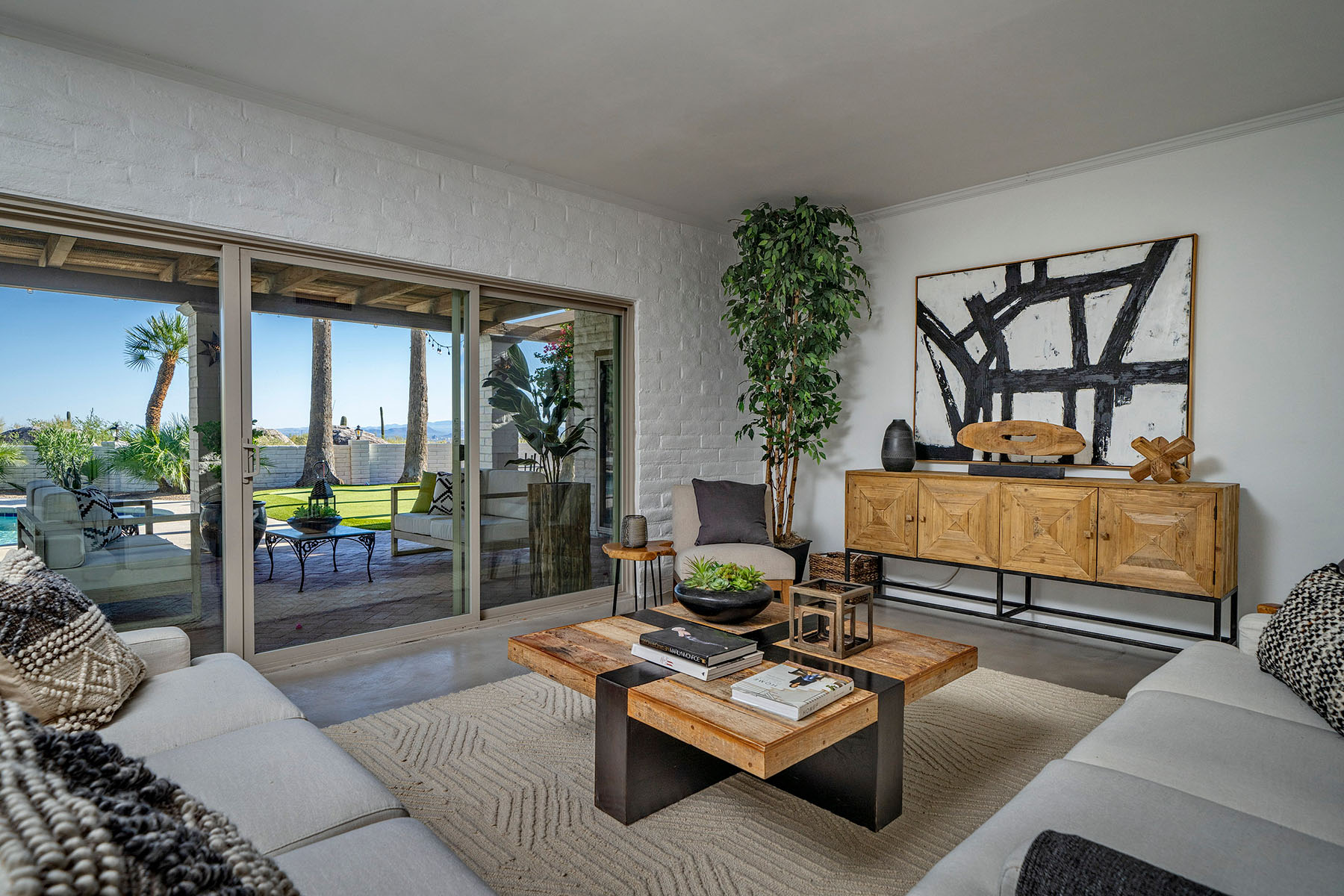 Professionally remodeled Tucson living room featuring white painted brick walls, polished concrete floors, large sliding glass doors, and seamless indoor outdoor living with mountain views and resort style backyard access