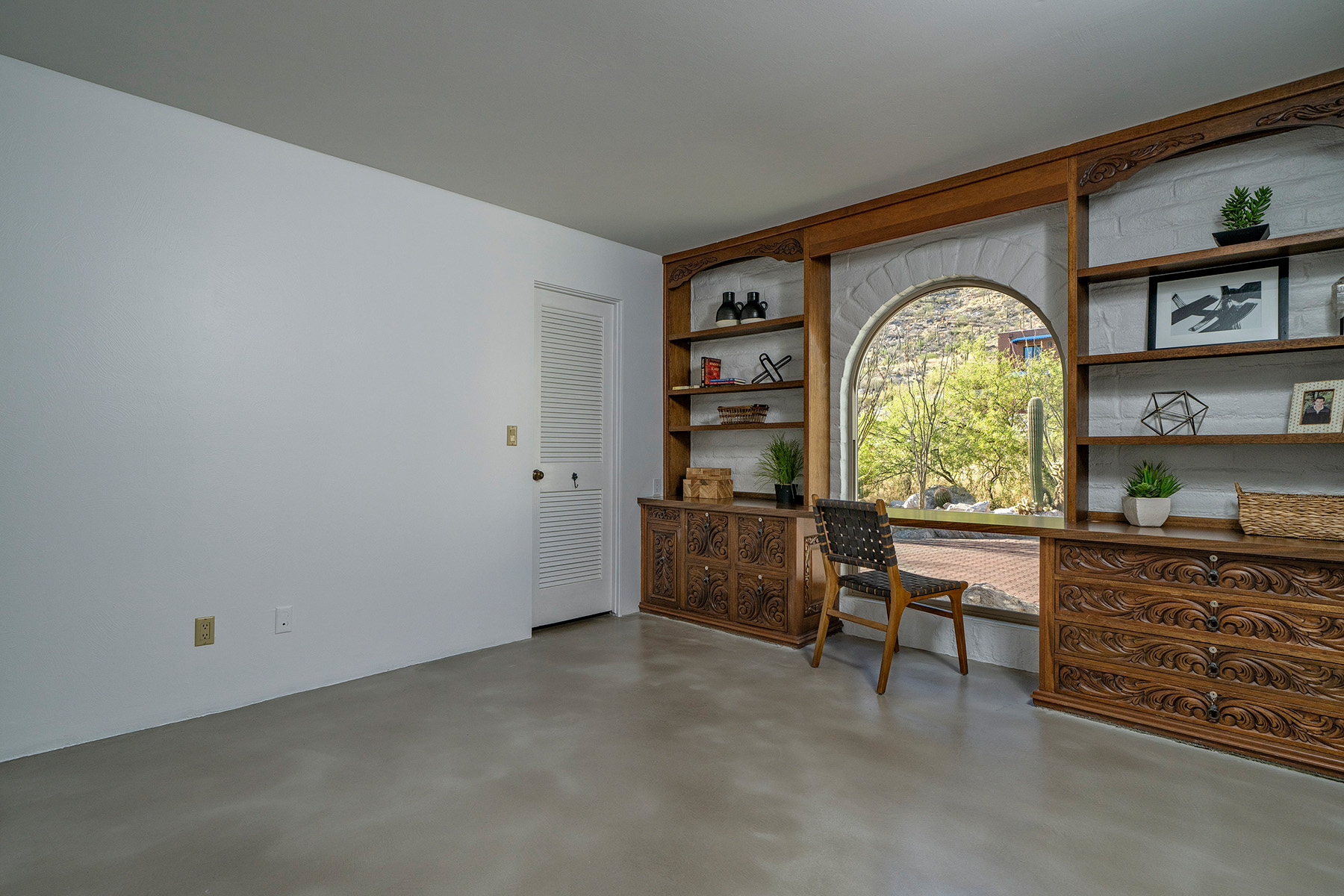 Spacious bonus room in a remodeled Tucson home featuring custom built in cabinetry, workspace, arched picture window, polished concrete flooring, and scenic desert views