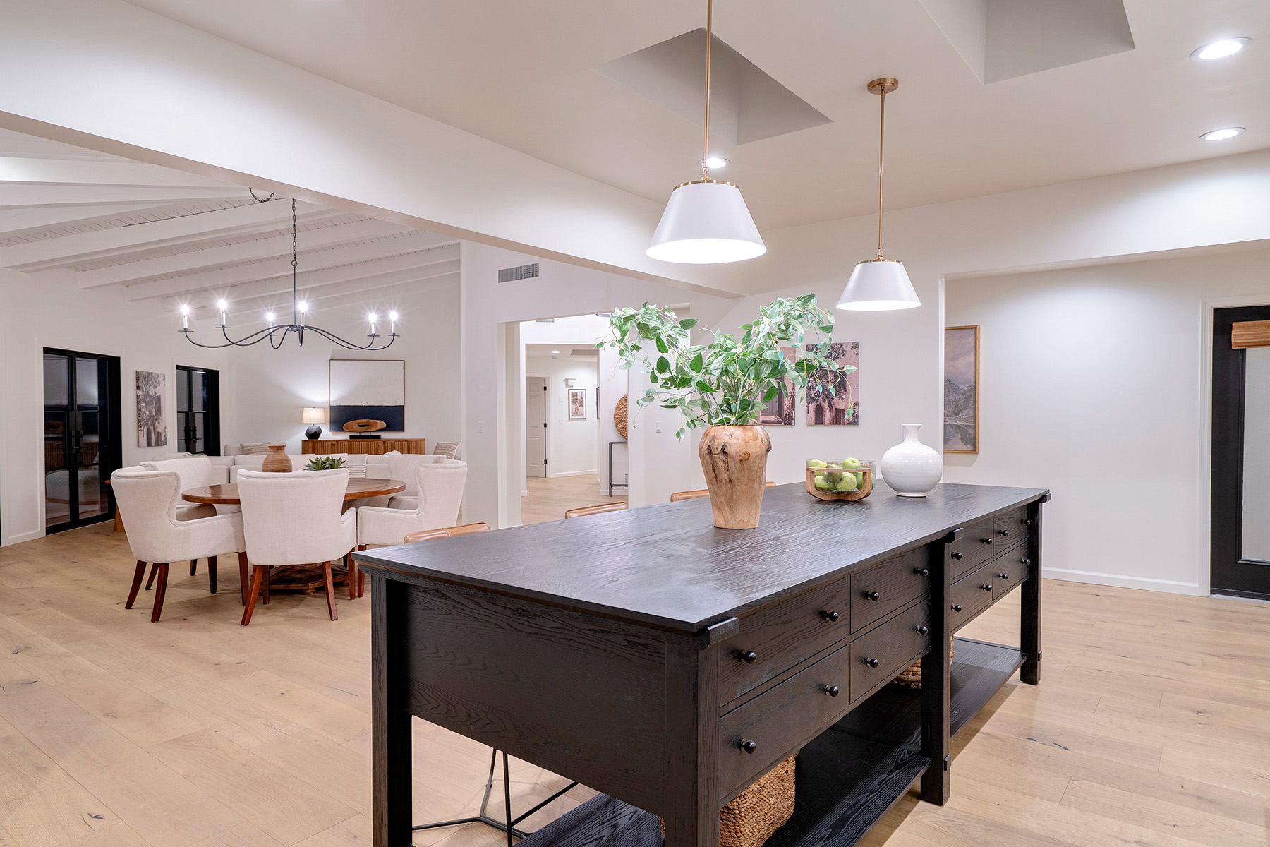 Spacious open-concept kitchen featuring a custom black island, designer lighting, white oak flooring, and seamless flow into adjacent living spaces