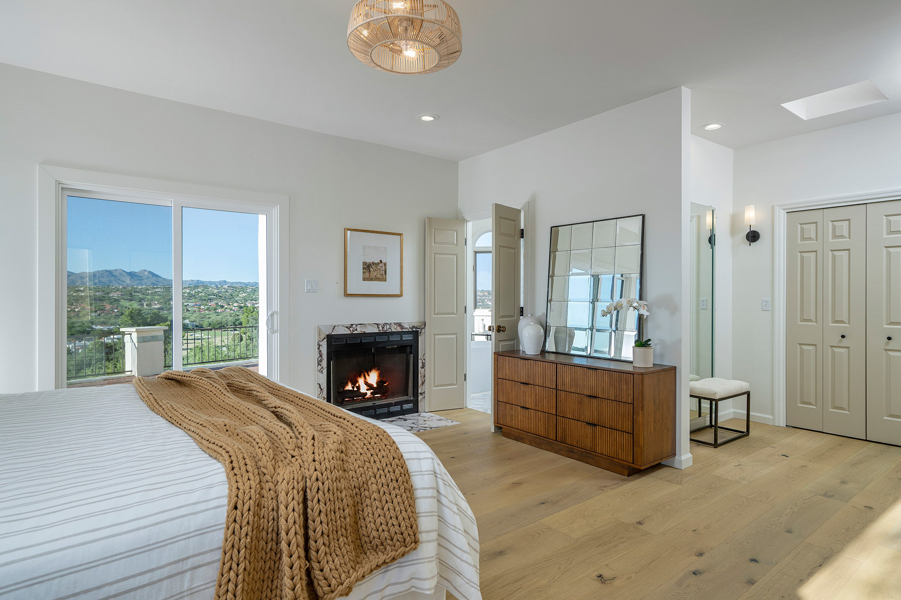 Primary bedroom retreat featuring a fireplace, expansive mountain views, white oak flooring, and a bright, inviting atmosphere