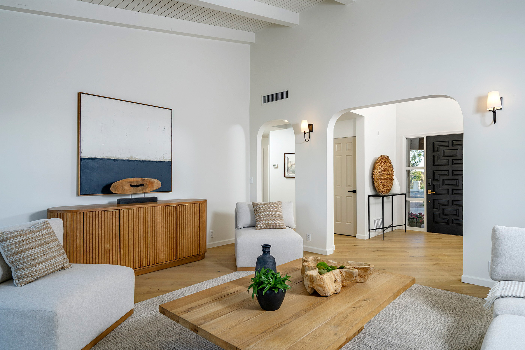 Modern living room with vaulted ceilings, custom millwork, natural wood furnishings, and a warm neutral color palette