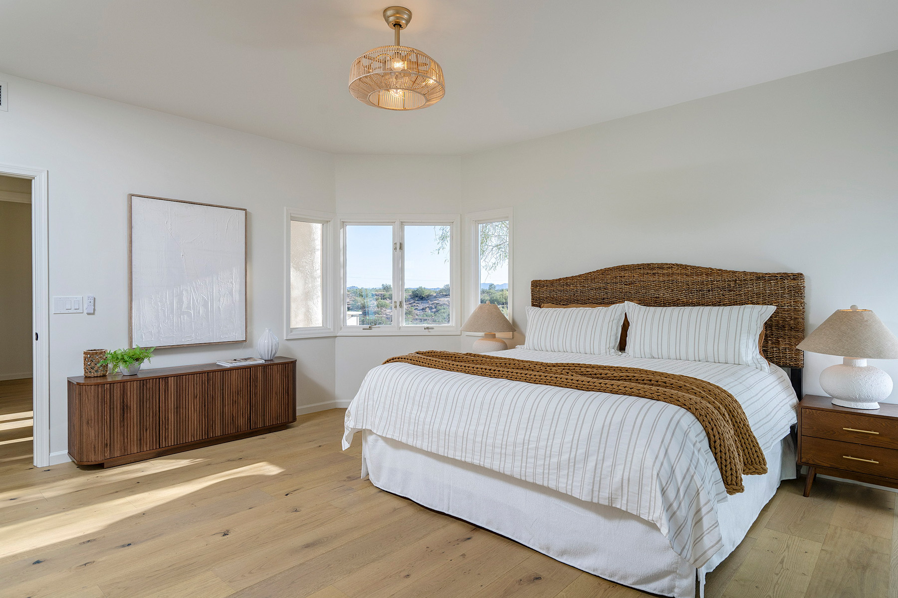 Elegant primary bedroom featuring custom furnishings, natural textures, abundant natural light, and views of the surrounding desert landscape