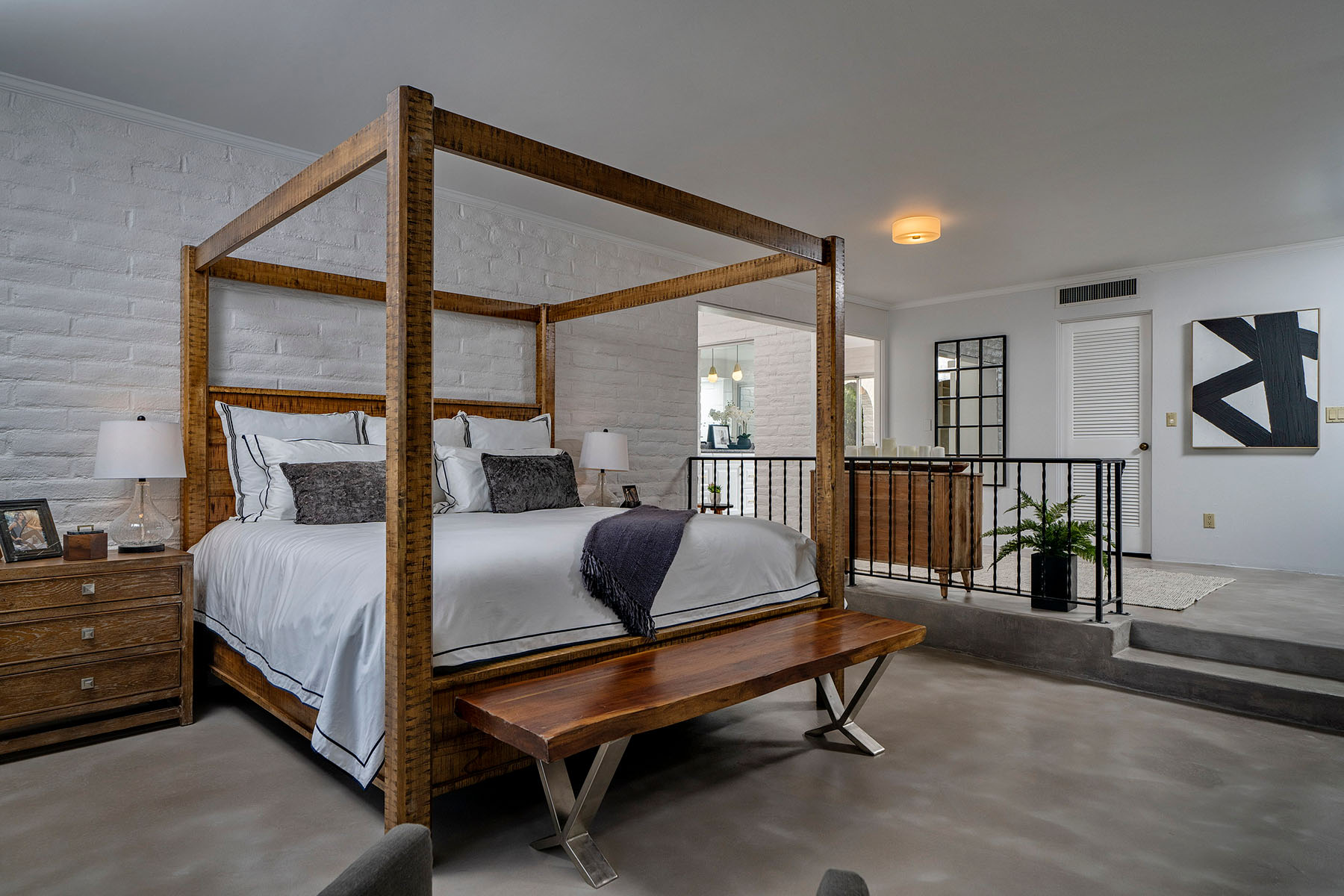 Large primary bedroom with polished concrete floors, custom canopy bed, white brick accents, and open layout designed for luxury desert living