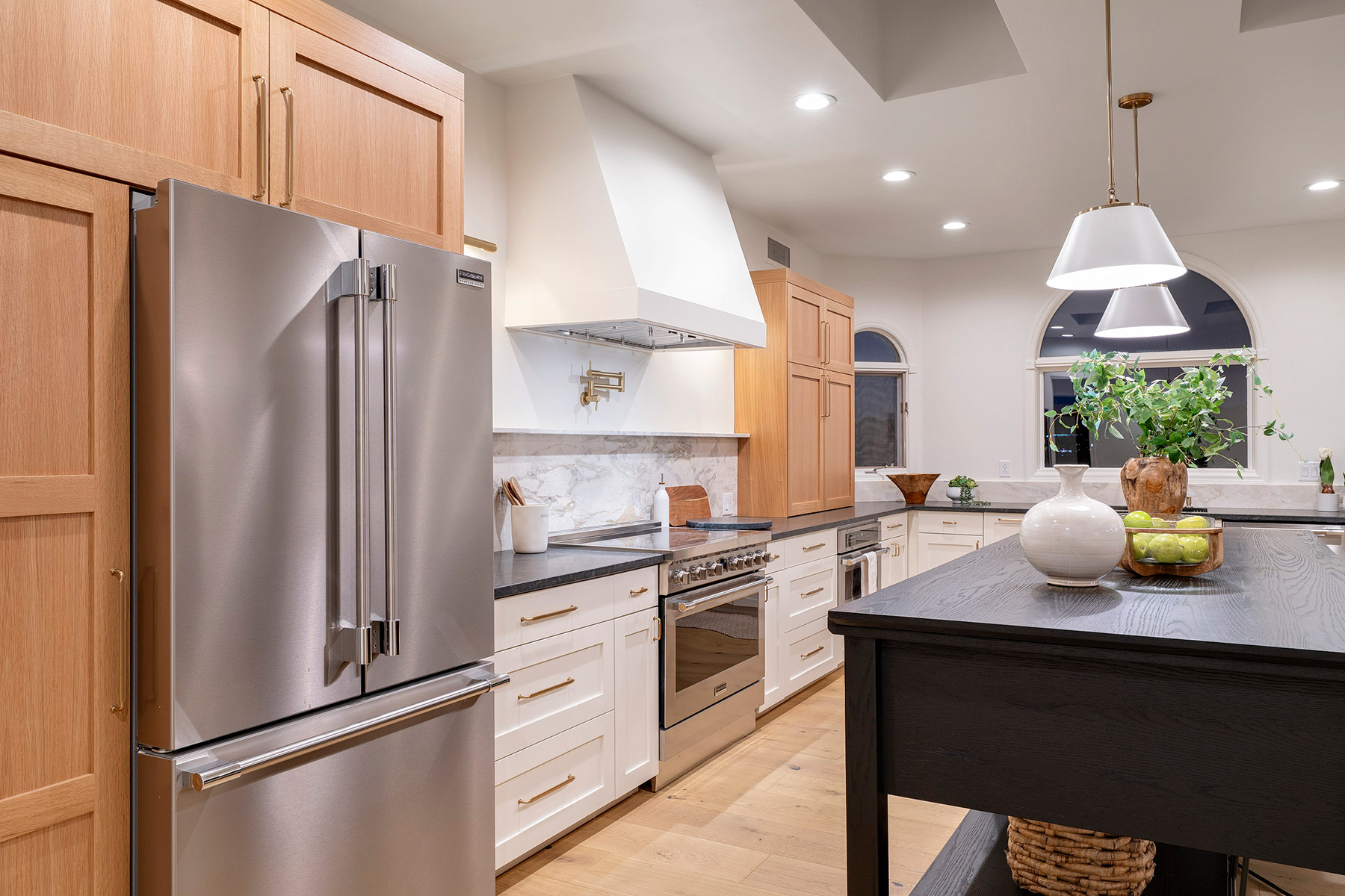 Thoughtfully designed kitchen with white oak cabinetry, custom range hood, stone backsplash, premium appliances, and designer finishes